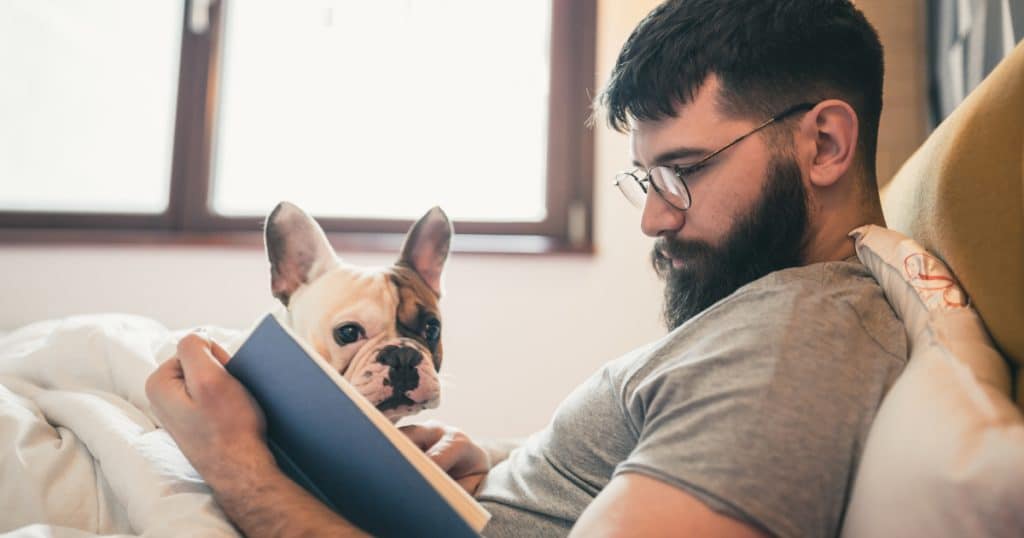 Man reading book in the bed, cuddling with his dog

