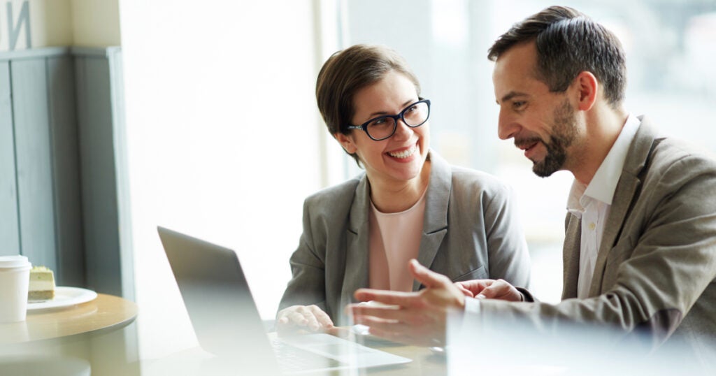 Two colleagues smile with computer